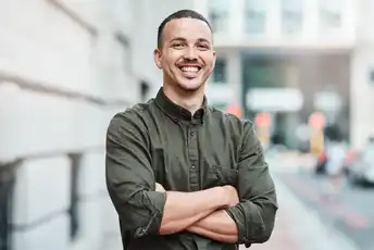 Man smiling confidently with arms crossed while standing outdoors on a city street.